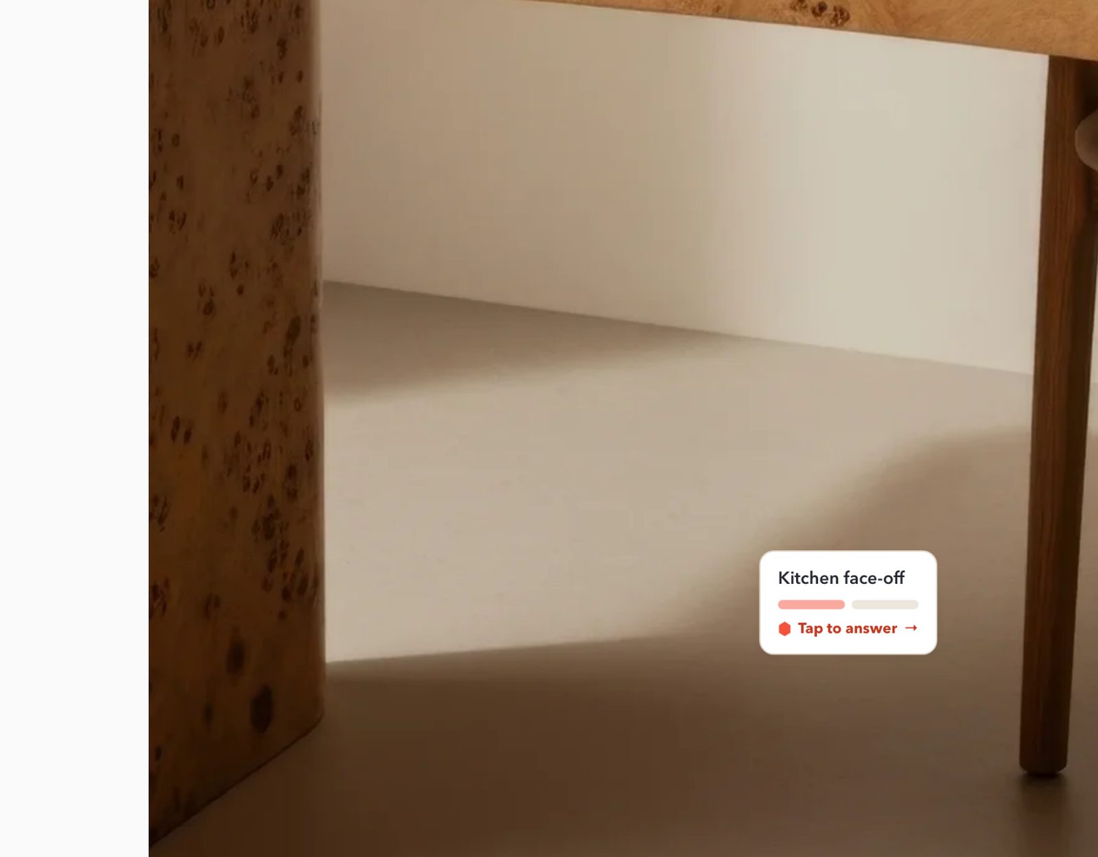 A close crop of the desk photo on the live Squarespace page, showing a table leg and the floor, with the Kitchen face-off mini card (Tap to answer) near its bottom-right corner